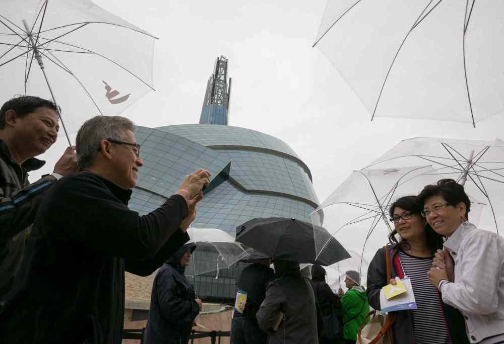 Melissa Tait / Winnipeg Free Press
Frank Yong snaps a photo of his wife, Teresa, and her friend Jenny Lee, all from British Columbia, while they wait in the rain for their preview tour at the Canadian Museum for Human Rights on Saturday. The rain kept away some of the people with reserved tickets, allowing walk-ups to gain access to the guided tour of four of 11 galleries. The rest of the galleries open to the public Sept. 27.
