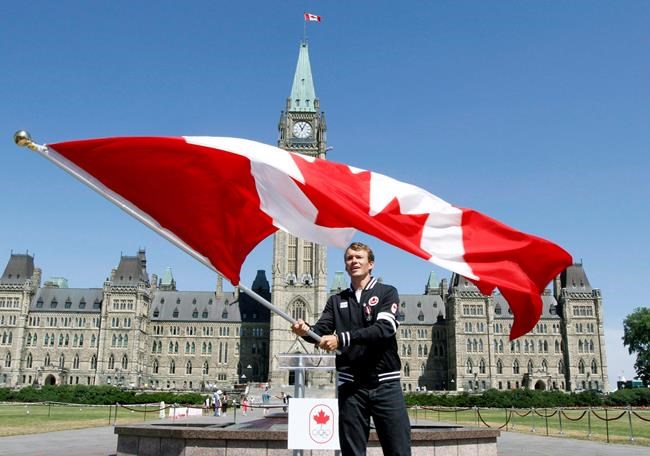 Triathlete Simon Whitfield of British Columbia waves the Canadian Flag after he was named the official flag bearer for the London Olympics during a ceremony on Parliament Hil on Thursday July 12 2012 in Ottawa. Four athletes, two teams, a coach and a pair of builders will be inducted into the Canadian Olympic Hall of Fame this year. THE CANADIAN PRESS/Fred Chartrand