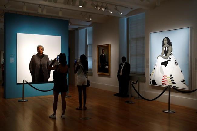 Visitors photograph a portrait of Nobel laureate Toni Morrison, painted by the artist Robert McCurdy, Tuesday, Aug. 6, 2019, near a portrait of former first lady Michelle Obama, painted by the artist Amy Sherald, at the National Portrait Gallery in Washington. (AP Photo/Patrick Semansky)