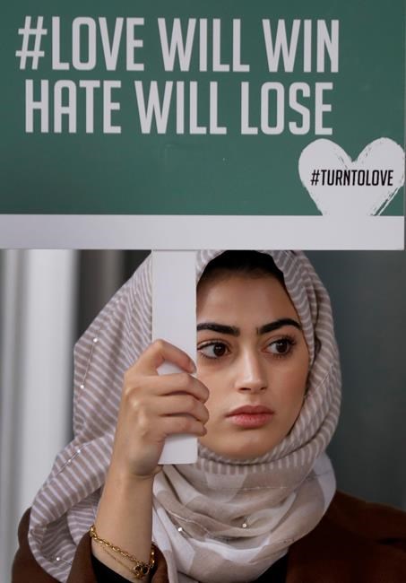 A demonstrator holds a banner from multi-faith group 'Turn to Love' during a vigil at New Zealand House in London, Friday, March 15, 2019. Multiple people were killed in mass shootings at two mosques full of worshippers attending Friday prayers on what the prime minister called