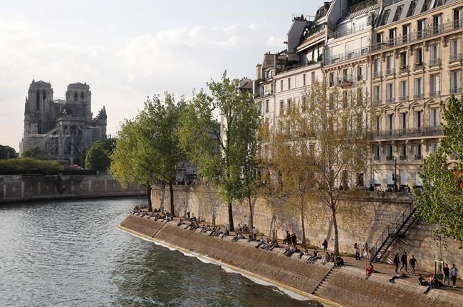 People enjoy the sun next the Notre Dame Cathedral along the Seine river in Paris, Friday, April 19, 2019. Rebuilding Notre Dame, the 800-year-old Paris cathedral devastated by fire this week, will cost billions of dollars as architects, historians and artisans work to preserve the medieval landmark. (AP Photo/Michel Euler)