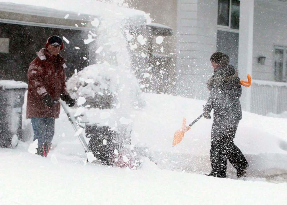 Kim Barrow, with yellow push shovel, is happy that her neighbour on Cormorant Bay, Bob Yamashita, has a gas powered snowblower. (Boris Minkevich / Winnipeg Free Press)