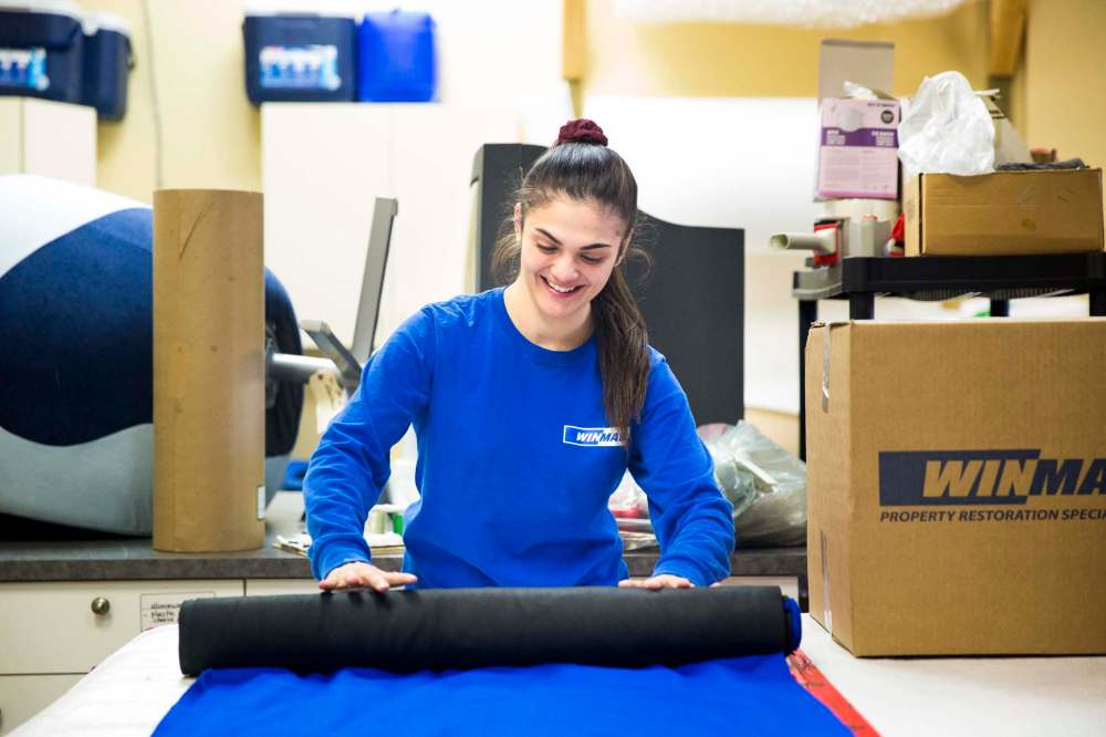 Sydney Daniel rolls up floor runners after a job.