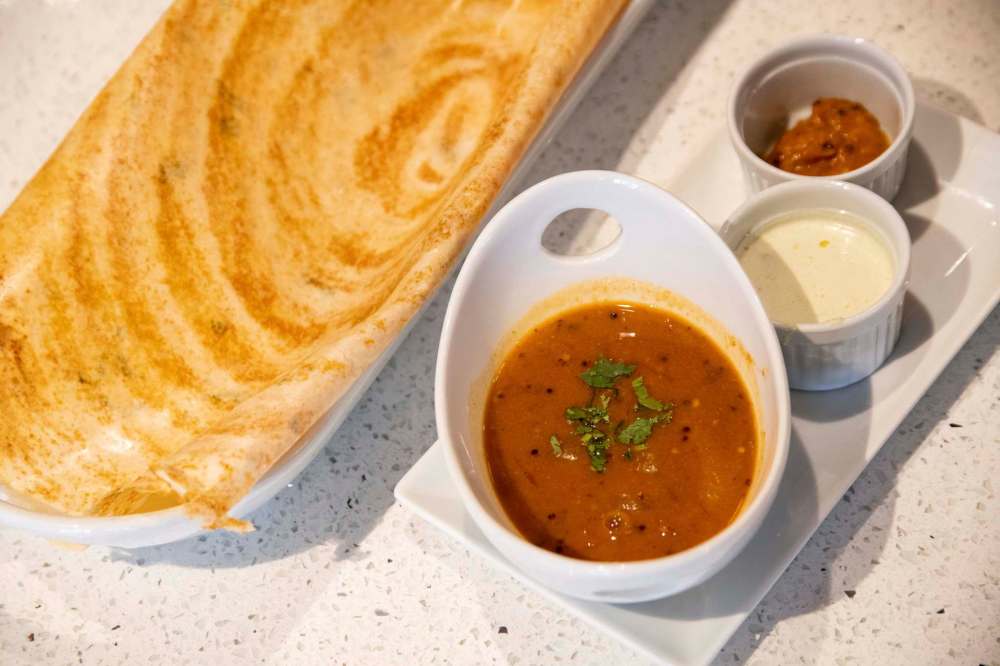 A plate of Masala Dosa, served with lentil soup and an assortment of dips.