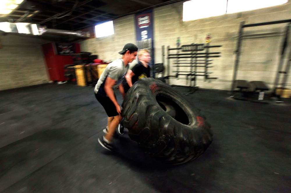 Cole Younger (left) and Easton Lewicki flip a giant tire around the Cross Fit 204 Gym. (Phil Hossack / Winnipeg Free Press)