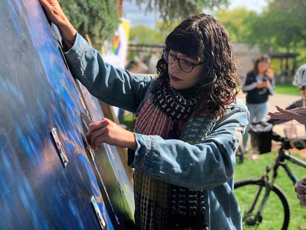Artist Ruby Rain pins a photo of a loved one lost to overdose on her painting of a tree at Recovery Day. (Tessa Vanderhart / Winnipeg Free Press)