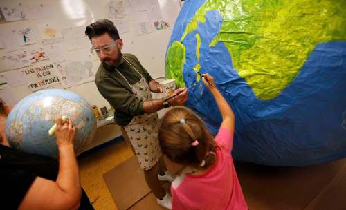 Art City&rsquo;s art director Eddy Ayoub (centre) looks for references on an actual globe, while 8-year-old Emma Loshakova paints Cuba on a giant paper mâché globe Tuesday afternoon preparing to participate in the Global Climate Strike to be held here on Friday. (Phil Hossack / Winnipeg Free Press)