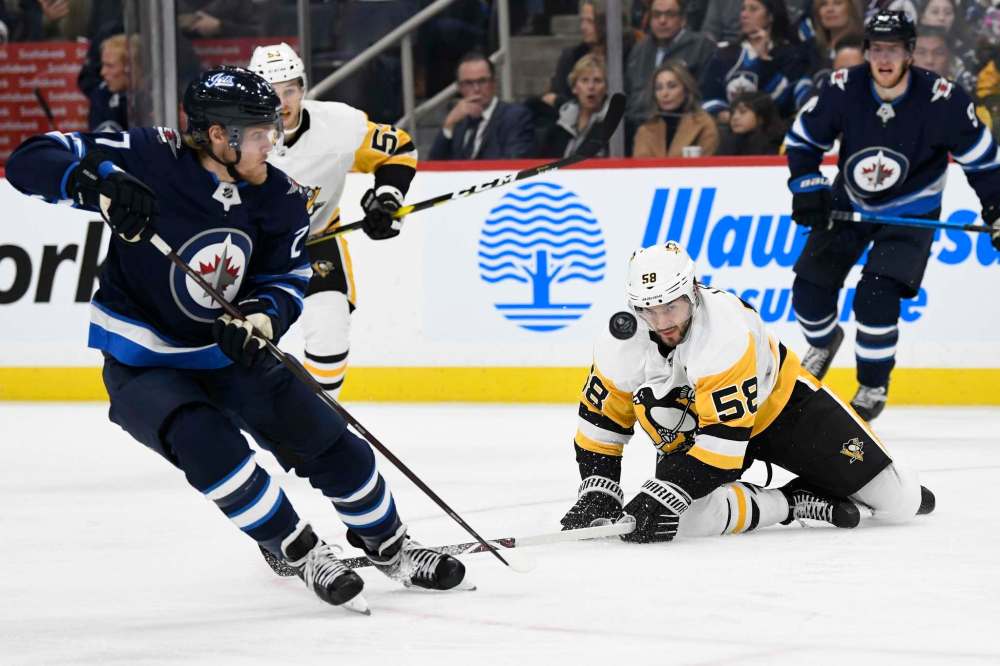 Pittsburgh Penguins' Kris Letang (58) keeps his eyes on the puck as Winnipeg Jets' Nikolaj Ehlers (27) skates down ice during first second NHL action in Winnipeg on Sunday, Oct. 13, 2019. THE CANADIAN PRESS/Fred Greenslade