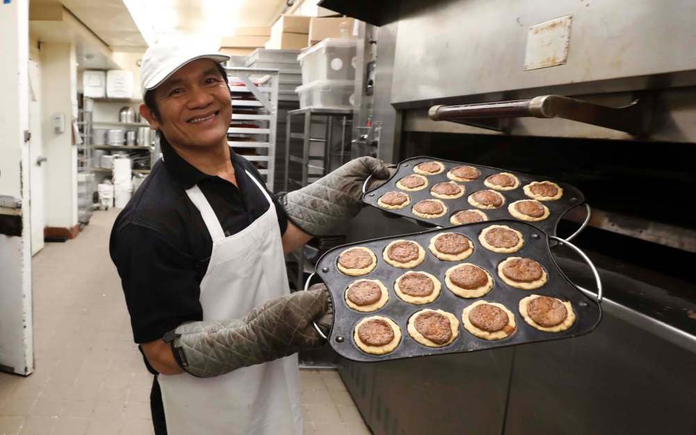 Cuomg Lam takes two out of many trays of butter tarts from the oven. (Ruth Bonneville / Winnipeg Free Press)