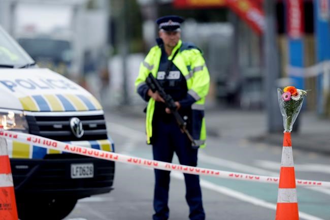 Flower rest at a road block, as a Police officer stands guard near the Linwood mosque, site of one of the mass shootings at two mosques in Christchurch, New Zealand, Saturday, March 16, 2019. (AP Photo/Mark Baker)
