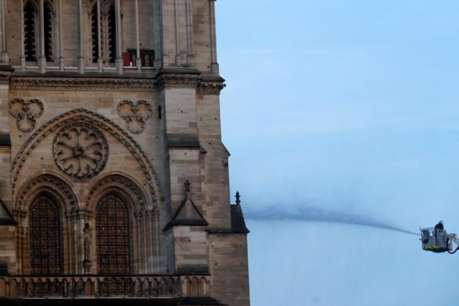 A fire fighter tackles the blaze as flames and smoke rise while Notre Dame cathedral is burning in Paris, Monday, April 15, 2019. A catastrophic fire engulfed the upper reaches of Paris' soaring Notre Dame Cathedral as it was undergoing renovations Monday, threatening one of the greatest architectural treasures of the Western world as tourists and Parisians looked on aghast from the streets below. (AP Photo/Francois Mori)