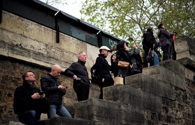 People stand to watch and photograph the Notre Dame cathedral after the fire in Paris, Tuesday, April 16, 2019. Experts are assessing the blackened shell of Paris' iconic Notre Dame cathedral to establish next steps to save what remains after a devastating fire destroyed much of the almost 900-year-old building. With the fire that broke out Monday evening and quickly consumed the cathedral now under control, attention is turning to ensuring the structural integrity of the remaining building. (AP Photo/Kamil Zihnioglu)