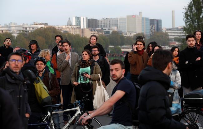 People watch as flames and smoke rise from Notre Dame cathedral as it burns in Paris, Monday, April 15, 2019. Massive plumes of yellow brown smoke is filling the air above Notre Dame Cathedral and ash is falling on tourists and others around the island that marks the center of Paris. (AP Photo/Thibault Camus)