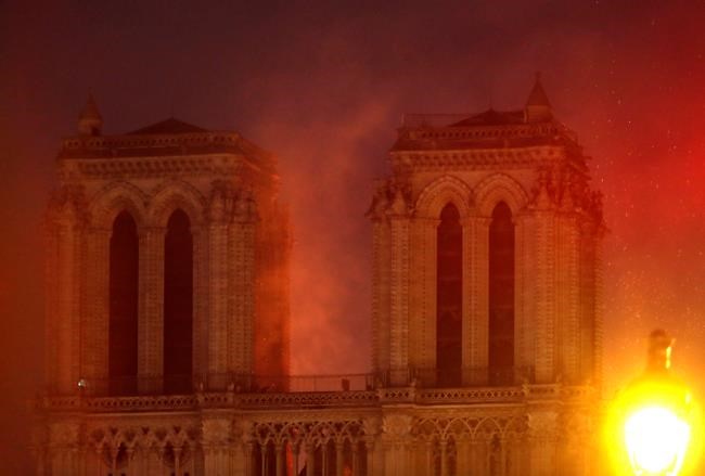 Flames illuminate the night sky as Notre Dame cathedral burns in Paris, Monday, April 15, 2019. Massive plumes of yellow brown smoke is filling the air above Notre Dame Cathedral and ash is falling on tourists and others around the island that marks the center of Paris. (AP Photo/Thibault Camus)