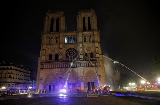 Firefighters spray water onto the facade of Notre Dame cathedral to stop the spread of a fire in Paris, Monday, April 15, 2019. Massive plumes of yellow brown smoke is filling the air above Notre Dame Cathedral and ash is falling on tourists and others around the island that marks the center of Paris. (AP Photo/Michel Euler)