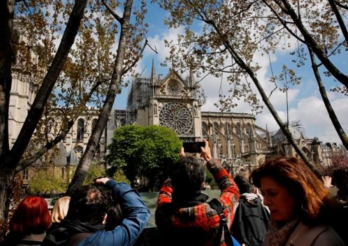 Tourists and others photograph the damage to the Notre Dame cathedral in Paris, Wednesday, April 17, 2019. Nearly $1 billion has already poured in from ordinary worshippers and high-powered magnates around the world to restore the Notre Dame cathedral in Paris after a massive fire. (AP Photo/Christophe Ena)
