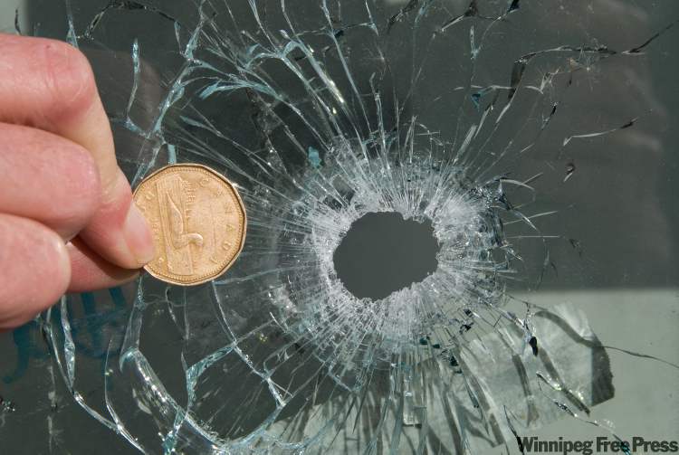 DAVID LIPNOWSKI / winnipeg free press
A loonie is shown beside a gunshot hole in a window of a suite in the 200 block of Stella Walk Sunday where a shooting took place.