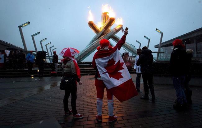 A woman draped in a Canadian flag and other fans gather at the Olympic cauldron as it was lit to commemorate the Canadian men's Olympic team win over Sweden in Vancouver, B.C., on February 23, 2014. City council is scheduled to consider a motion today on whether Vancouver should make a bid for the 2030 Winter Olympics. Coun. Melissa De Genova put the motion forward earlier this year but it was knocked off the agenda by the COVID-19 pandemic. THE CANADIAN PRESS/Darryl Dyck