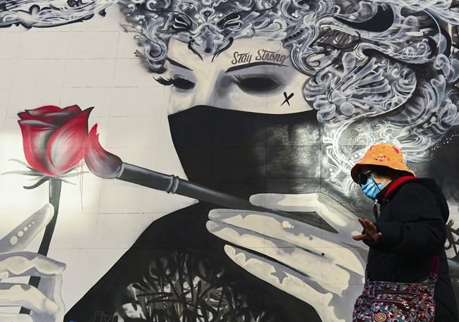 A woman wearing a protective mask walks past a face mask mural during the COVID-19 pandemic in Toronto on Thursday, November 12, 2020. THE CANADIAN PRESS/Nathan Denette