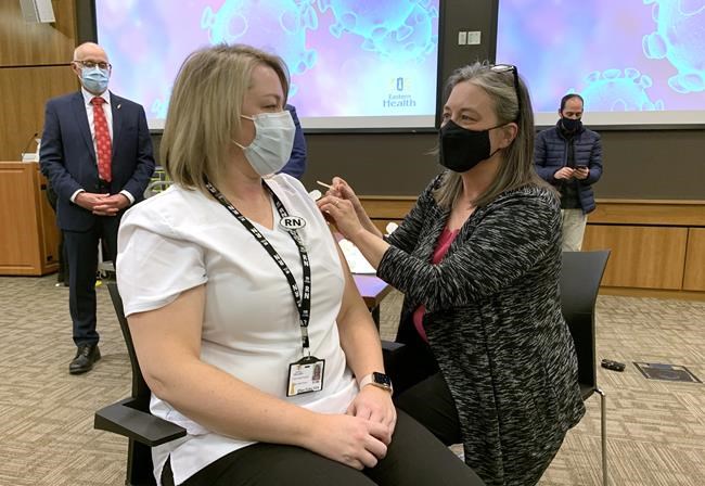 Newfoundland and Labrador's chief medical officer of health, Dr. Janice Fitzgerald, smiles at St. John's public health nurse Ellen Foley-Vick as she puts a bandage on her arm after giving her the Pfizer-BioNTech COVID-19 vaccine in St. John's, N.L., on Wednesday, Dec. 16, 2020. Foley-Vick is the first person in Newfoundland and Labrador to receive the Pfizer-BioNTech COVID-19 vaccine. THE CANADIAN PRESS/Sarah Smellie