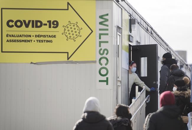 A healthcare worker talks with people as they wait to be tested for COVID-19 at a clinic in Montreal, Sunday, Dec. 27, 2020. A total of 15,001 Canadians have now died from COVID-19 since the pandemic began earlier this year. THE CANADIAN PRESS/Graham Hughes