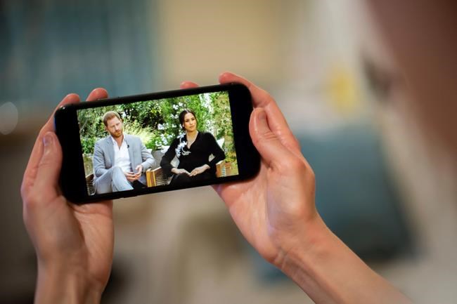 A man watches a phone screen showing an interview of Prince Harry and Meghan, The Duchess of Sussex, by Oprah Winfrey, in London Monday, March 8, 2021. THE CANADIAN PRESS/Aaron Chown/PA via AP