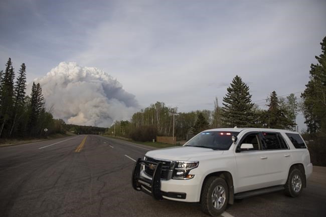 A Prince Albert police car is parked on Highway 55 as a plume of smoke rise from a forest fire burning northeast of the city in Prince Albert, Sask., Monday, May 17, 2021. The Saskatchewan Public Safety Agency has revoked a fire ban as cooler temperatures begin to prevail in the province. THE CANADIAN PRESS/Kayle Neis