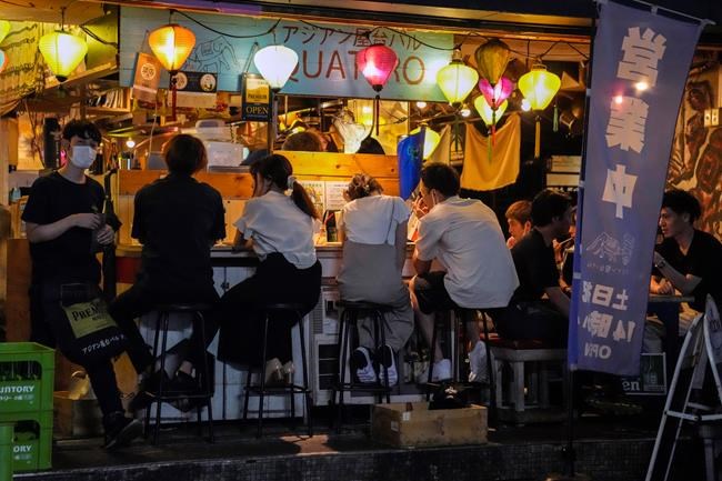 People gather at a bar after government imposed 8 p.m. closing time for restaurants and bars under Tokyo's fourth state of emergency Saturday, July 17, 2021, in Tokyo. The latest state of emergency has asked restaurants and bars to close by 8 p.m., if not entirely. This has pushed people to drink outside, although many bars remain open and bustling with customers who are defying the rules and expressing frustration and indifference. (AP Photo/Kiichiro Sato)