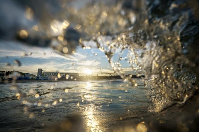 A wave breaks at Tsurigasaki beach as the venue for the surfing competition at the Tokyo 2020 Olympics stands in the background in Ichinomiya, Japan, Wednesday, July 21, 2021. (AP Photo/David Goldman)
