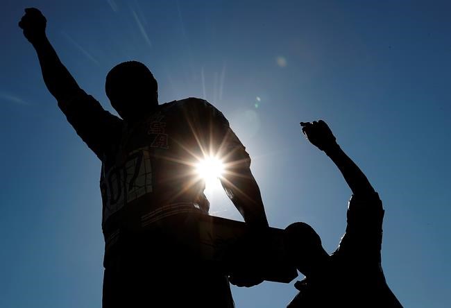 FILE - In this Oct. 17, 2018, file photo, a statue in honor of former Olympians Tommie Smith, left, and John Carlos is seen on the campus of San Jose State University in San Jose, Calif. Smith and Carlos raised their black-gloved fists while their national anthem played during the 200-meters medals ceremony at the Mexico City Olympics in 1968. Rule 50 of the IOC charter states: “No kind of demonstration or political, religious or racial propaganda is permitted in any Olympic sites, venues or other areas.” (AP Photo/Tony Avelar, File)