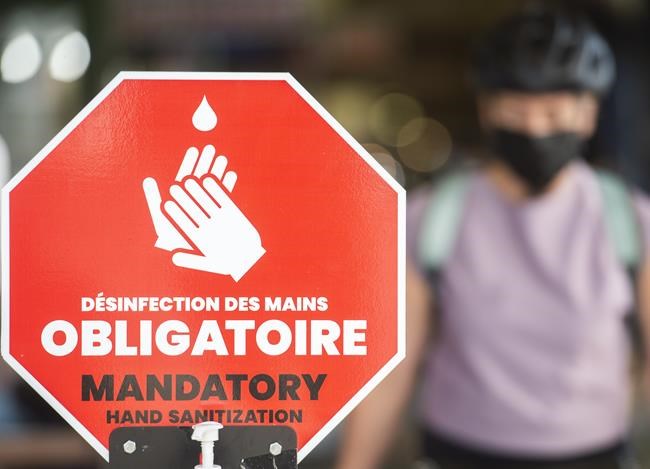 People wear face masks as they walk by a sign reading