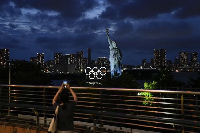 A woman takes pictures of the Olympic rings mounted on a barge floating in the water near a replica of the Statue of Liberty during the 2020 Summer Olympics, Thursday, July 29, 2021, in Tokyo, Japan. (AP Photo/Jae C. Hong)