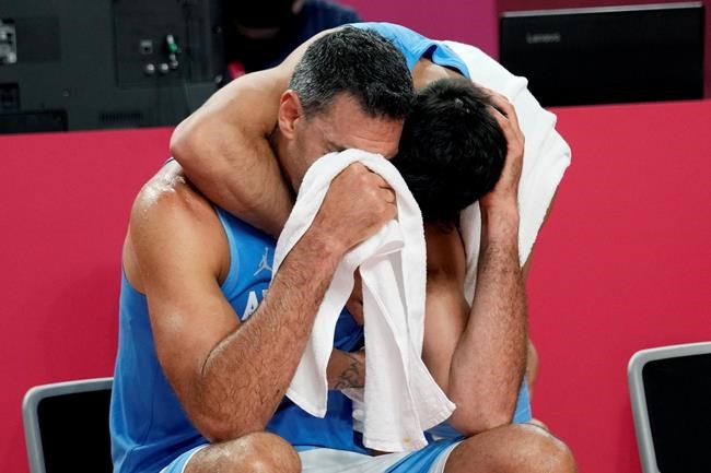 Argentina's Luis Scola (4) is hugged by teammate Facundo Campazzo as he receives an emotional standing ovation from his team, Australia players, and others in attendance when he was pulled from the game in the final moments of a men's basketball quarterfinal round game at the 2020 Summer Olympics, Tuesday, Aug. 3, 2021, in Saitama, Japan. (AP Photo/Eric Gay)