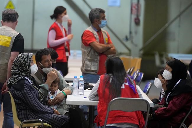 Afghans sit with a Red Cross worker in a COVID testing center after arriving on a Spanish Air Force plane carrying Spanish nationals and Afghans at the Torrejon military base as part of the evacuation process in Madrid, Spain, Thursday, Aug. 19, 2021. (AP Photo/Paul White)