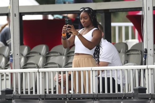 FILE - Olympic gymnast Simone Biles takes photos with her phone as she watches the Houston Texans practice at NFL football training camp in Houston, Friday, Aug. 6, 2021. Biles is at peace with her decision to opt out of several competitions at the Tokyo Olympics to focus on her mental health. The seven-time Olympic medalist is happy to spread the importance of putting the person ahead of the athlete, one of the themes of her fall exhibition tour that will feature four other members of the 2021 Olympic gymnastics team(Brett Coomer/Houston Chronicle via AP, File)