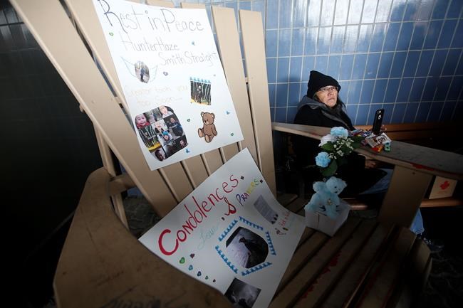A woman sits beside posters of Hunter Haze Smith-Straight at a vigil outside Winnipeg's Childrens Hospital, Friday, Nov. 1, 2019. THE CANADIAN PRESS/John Woods