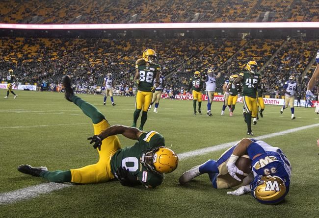 Winnipeg Blue Bombers' Andrew Harris (33) scores a touchdown as Edmonton Elks' Jonathan Rose (0) tries to stop him during first half CFL action in Edmonton on Friday, Oct. 15, 2021. The Winnipeg Blue Bombers will have to try and clinch top spot in the West Division standings Saturday without running back Andrew Harris. THE CANADIAN PRESS/Jason Franson.