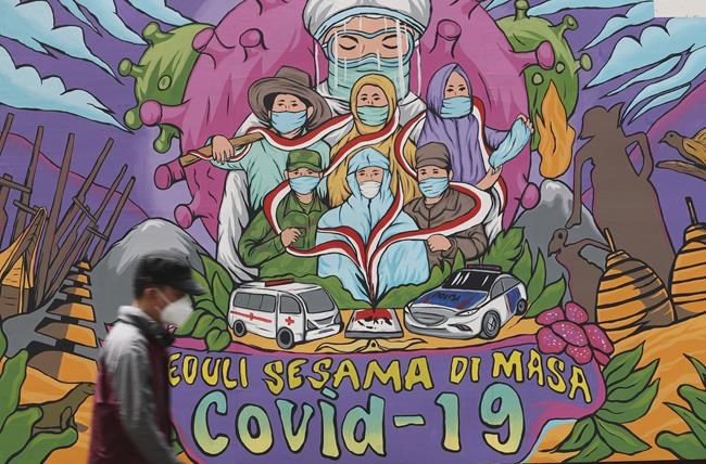 A man walks past a coronavirus-themed mural in Jakarta, Indonesia, Monday, Nov. 29, 2021. Cases of the omicron variant of the coronavirus popped up in countries on opposite sides of the world and many governments rushed to close their borders even as scientists cautioned that it's not clear if the new variant is more alarming than other versions of the virus. (AP Photo/Tatan Syuflana)