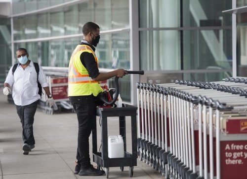 A man uses a sanitizer spray to wash down luggage carts at Toronto's Pearson International Airport&nbsp; in Toronto on Tuesday, June 23, 2020.&nbsp;Prime Minister Justin Trudeau says people will have to be careful as they finalize their Christmas plans this year, now that the highly transmissible Omicron variant is spreading through Canada. THE CANADIAN PRESS/Nathan Denette