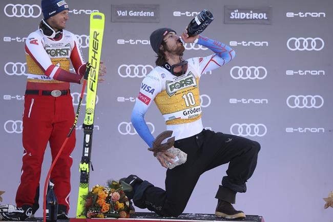 Second placed Austria's Otmar Striedinger, left, watches the winner United States' Bryce Bennett celebrate on podium after an alpine ski, men's World Cup downhill race, in Val Gardena, Italy, Saturday, Dec.18, 2021. (AP Photo/Alessandro Trovati)
