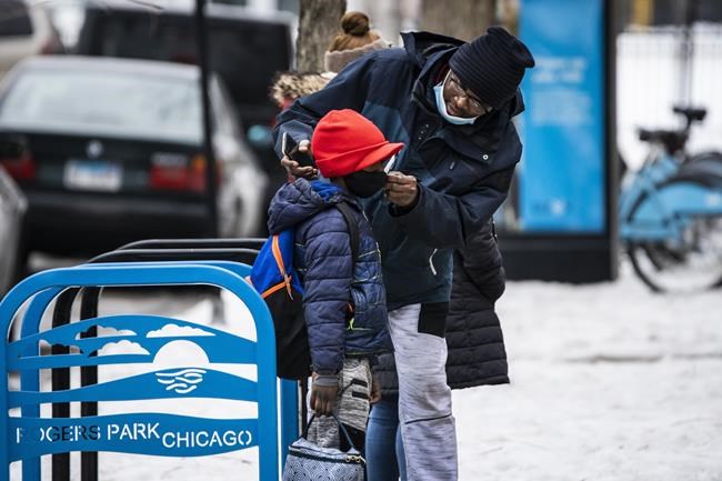 A man adjusts a boy's face mask as they arrive at Jordan Community Public School in Rogers Park on the North Side, Wednesday, Jan. 12, 2022 in Chicago. Students returned to in-person learning Wednesday after a week away while the Chicago Public Schools district and the Chicago Teachers Union negotiated stronger COVID-19 protections. (Ashlee Rezin /Chicago Sun-Times via AP)