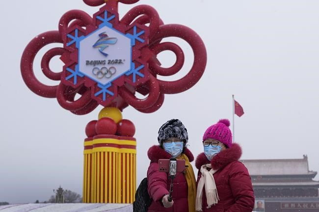 Women wearing face masks printed with a slogan for Beijing Winter Olympics Games take a selfie with a decoration for the Winter Olympics Games on Tiananmen Square in Beijing, Thursday, Jan. 20, 2022. With just over two weeks before the opening of the Beijing Winter Olympics, residents of the Chinese capital say they're disappointed at not being able to attend events because of coronavirus restrictions that have seen parts of the city placed under lockdown. (AP Photo/Andy Wong)