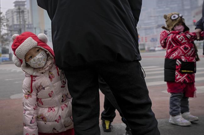 Children wearing face masks to help protect from the coronavirus stand with relatives waiting to cross a traffic intersection in the Central Business District of Beijing, Monday, Jan. 24, 2022. A fresh outbreak in Beijing has prompted authorities to test millions and impose new measures two weeks ahead of the opening of the Winter Olympics, even as Chinese officials on Monday lifted a monthlong lockdown on the northern city of Xi