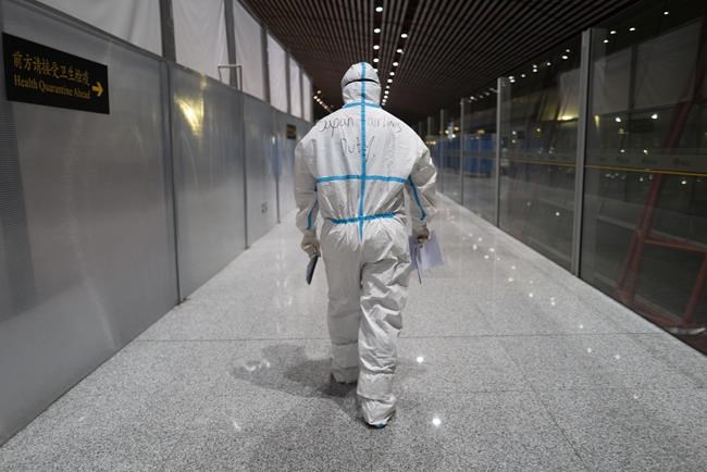 FILE - A member of airport personnel dressed in protective gear leads passengers into the customs area at the Beijing Capital International Airport ahead of the 2022 Winter Olympics in Beijing, Jan. 24, 2022. (AP Photo/Jae C. Hong, File)