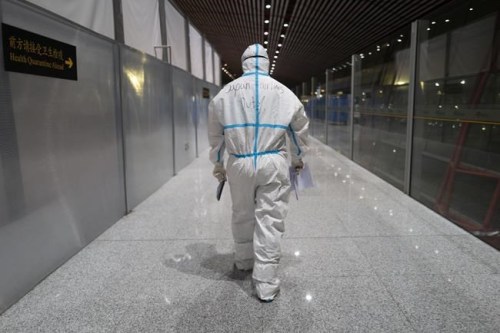 FILE - A member of airport personnel dressed in protective gear leads passengers into the customs area at the Beijing Capital International Airport ahead of the 2022 Winter Olympics in Beijing, Jan. 24, 2022. (AP Photo/Jae C. Hong, File)