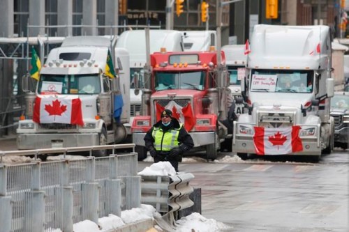 A police member stands in front of trucks blocking downtown streets as a rally against COVID-19 restrictions, which began as a cross-country convoy protesting a federal vaccine mandate for truckers, continues in Ottawa, on Wednesday, February 9, 2022. THE CANADIAN PRESS/ Patrick Doyle