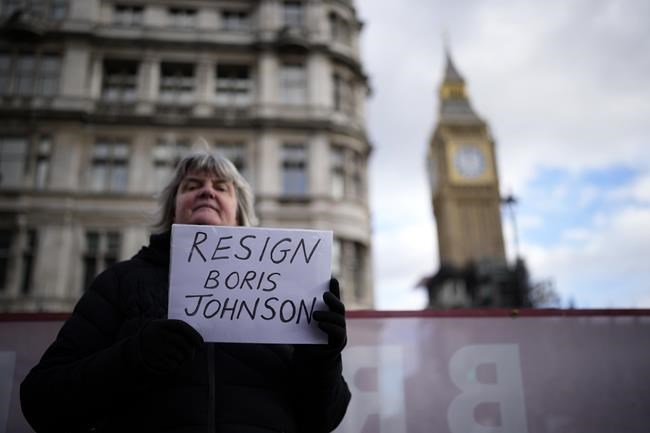 An anti-Boris Johnson protester holds up a placard calling on him to resign, backdropped by the Elizabeth Tower, known as Big Ben, of the Houses of Parliament, in London, Wednesday, Feb. 9, 2022. Boris Johnson has brought in new senior staffers as he tries to restore his flagging authority — including a communications chief who insisted the British prime minister is