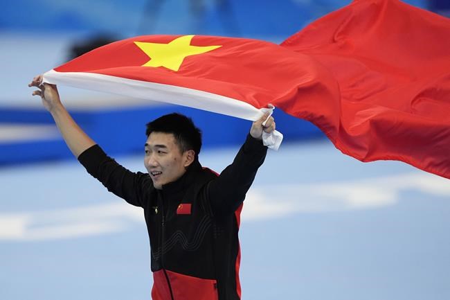 Tingyu Gao of China carries his country's flag after winning the gold medal and setting an Olympic record in the men's speedskating 500-meter race at the 2022 Winter Olympics, Saturday, Feb. 12, 2022, in Beijing. (AP Photo/Ashley Landis)