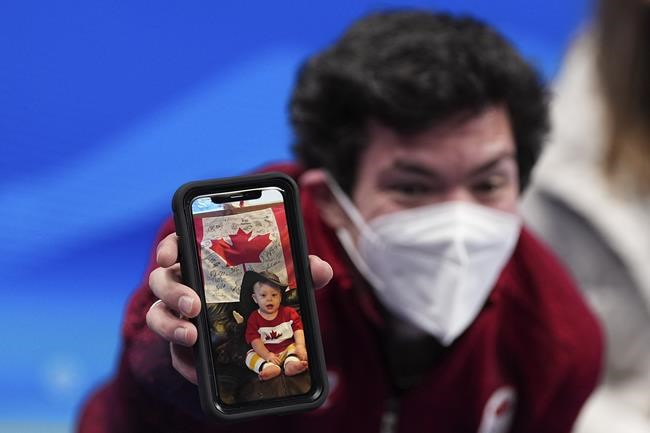 Keegan Messing, of Canada, holds up a photo of his baby after competing in the men's free skate program during the figure skating event at the 2022 Winter Olympics, Thursday, Feb. 10, 2022, in Beijing. (AP Photo/David J. Phillip)