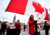 Women drum as they pass under a giant Canadian flag in front of Parliament Hill on the 20th day of a protest against COVID-19 measures that has grown into a broader antigovernment protest, in Ottawa, on Wednesday, Feb. 16, 2022. THE CANADIAN PRESS/Justin Tang